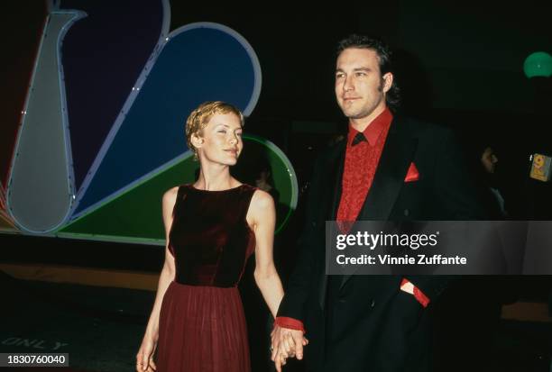 American actress Janine Turner, with blonde hair, wearing a sleeveless deep red evening gown, and American actor John Corbett, who wears a black...