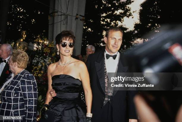 American actor and film director Kevin Costner, wearing a tuxedo and bow tie, and his wife, Cindy Silva, who wears a black off-shoulder outfit and...