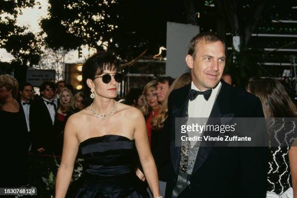 American actor and film director Kevin Costner, wearing a tuxedo and bow tie, and his wife, Cindy Silva, who wears a black off-shoulder outfit and...