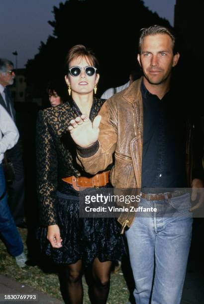American actor and film director Kevin Costner, wearing a brown leather jacket over a black shirt, with his wife, Cindy Silva, who wears a...