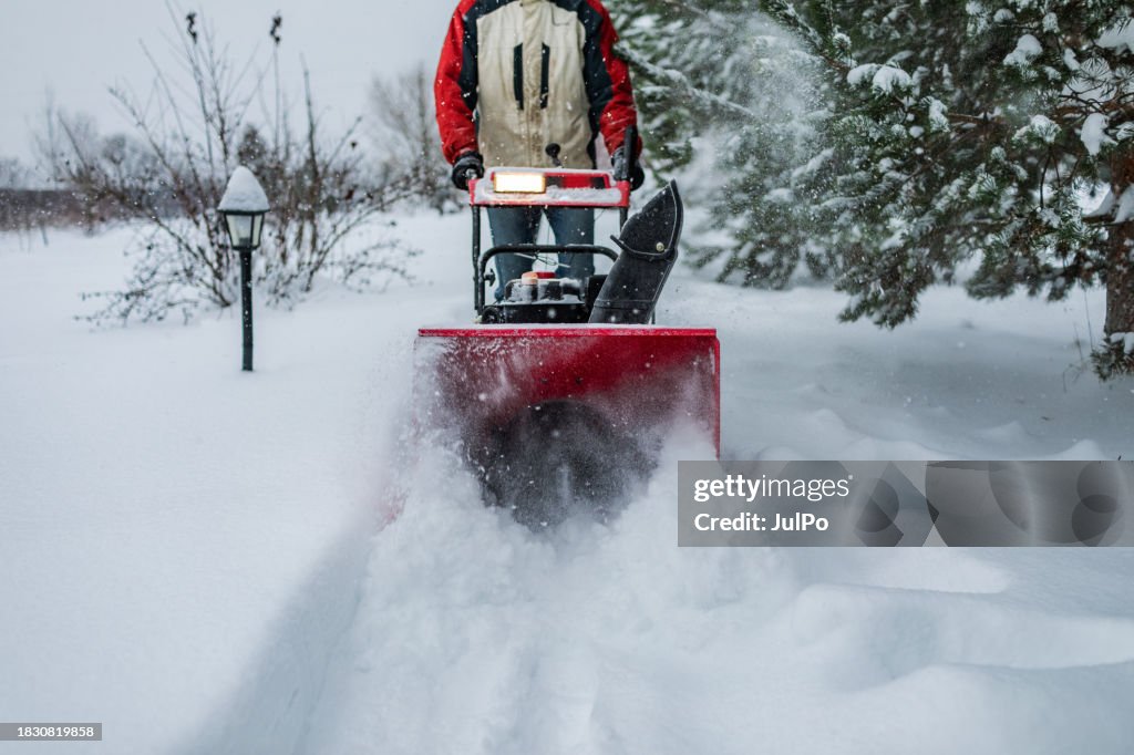 Adult man removing snow with snowblower at heavy snowfall