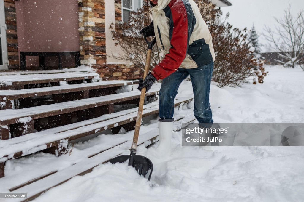 Erwachsener Mann räumt Schnee von der Veranda mit Schaufel