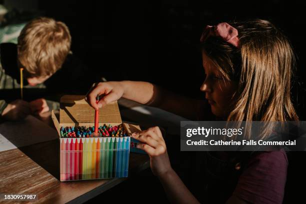a child chooses a red crayon out of a large box of multicoloured wax crayons - sketch pen stock pictures, royalty-free photos & images