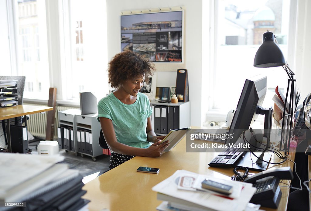 Woman sitting at creative desk scrolling on tablet