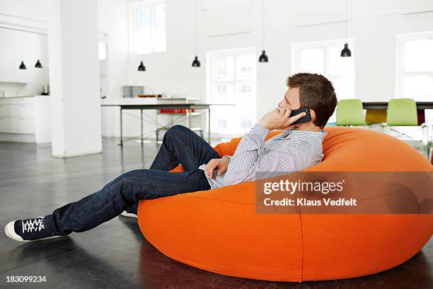 man lying on beanbag talking on smartphone - beanbag chair stockfoto's en -beelden
