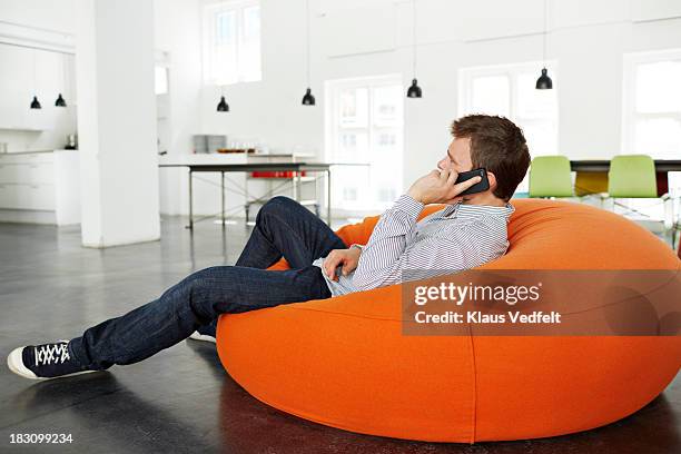 man lying on beanbag talking on smartphone - bean bags stock pictures, royalty-free photos & images