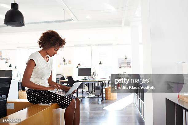businesswoman sitting on counter typing on laptop - laptop netbook fotografías e imágenes de stock