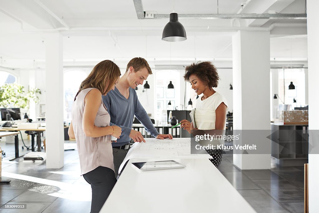 Creative coworkers discussing over blueprints