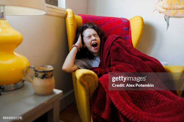 yawning woman struggling from insomnia, trying to take a nap during the day, wrapped in a blanket in the armchair in the living room - yawning stock pictures, royalty-free photos & images