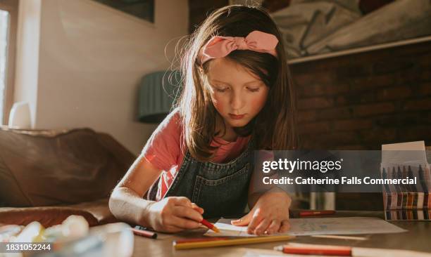 a cute young girl concentrates as she carefully writes with a wax crayon on a sheet of paper - sketch pen stock pictures, royalty-free photos & images