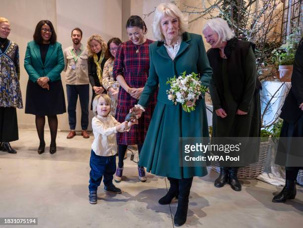 Queen Camilla and 3-years-old Max Woodward play tug of war over his toy dinosaur during the opening of the Winter Flower Week at the Garden Museum on...