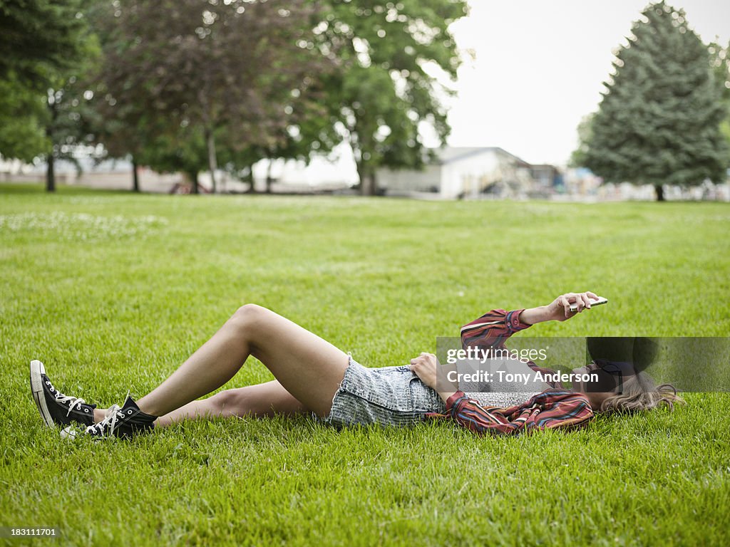 Young woman lying on grass in park with mobile