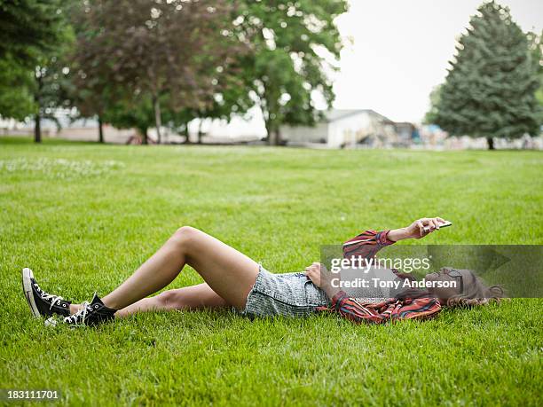 young woman lying on grass in park with mobile - laying park stock pictures, royalty-free photos & images