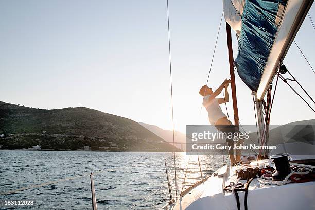 man hoisting sail, backlit - mezzo di trasporto marittimo foto e immagini stock