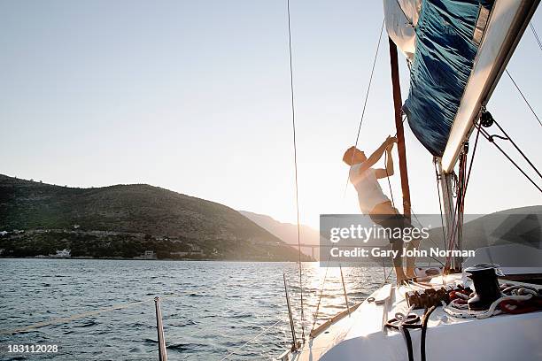 man hoisting sail, backlit - zeil stockfoto's en -beelden