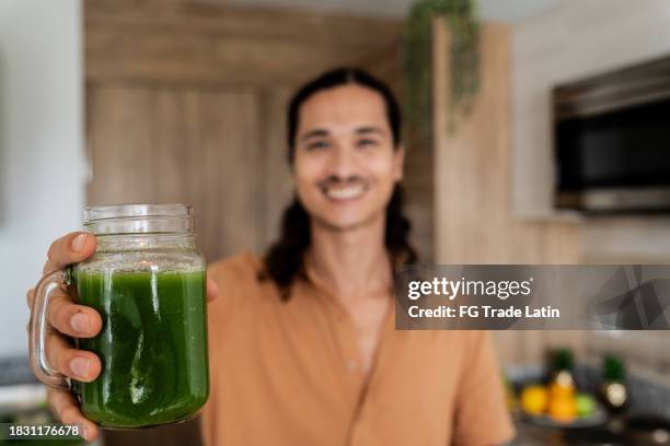 nahaufnahme eines mannes, der ein glas entgiftungssaft in der küche zu hause hält - smoothie close up textfreiraum stock-fotos und bilder