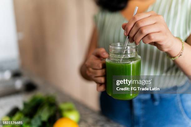 nahaufnahme einer frau, die einen entgiftungssaft in der hand hält und ihn zu hause mischt - smoothie close up textfreiraum stock-fotos und bilder