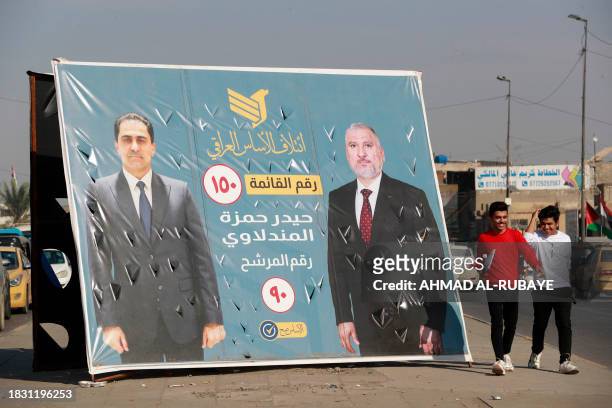 People walk past an electoral billboard in Baghdad on December 7 as Iraqis prepare to vote on December 18 to select councils in more than a dozen...