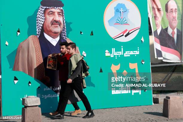 People walk past electoral billboards in Baghdad on December 7 as Iraqis prepare to vote on December 18 to select councils in more than a dozen...
