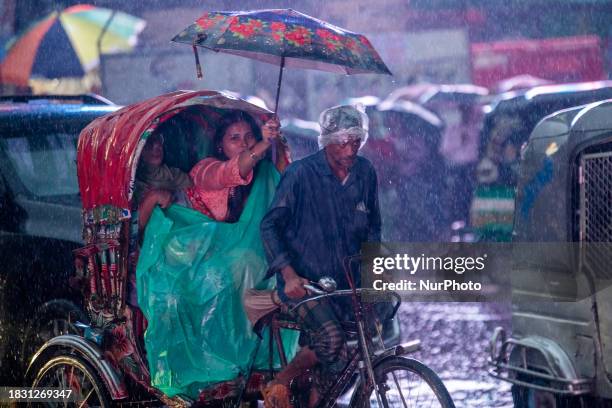 Passenger is holding an umbrella to shield her rickshaw puller from the rain in Dhaka, Bangladesh, on December 7, 2023. The Bangladesh Meteorological...