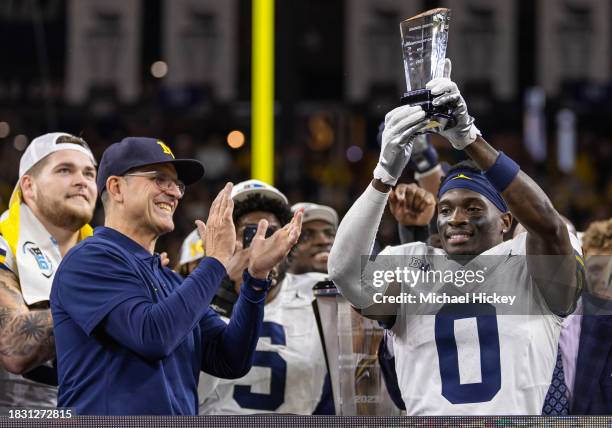 Head coach Jim Harbaugh applauds as Mike Sainristil of the Michigan Wolverines holds up the MVP trophy following the Big Ten Championship against the...