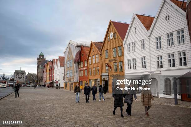Several people are walking along a street next to the Bredsgarden Building, a historic wooden building from the 18th century, in Bergen, Norway, on...
