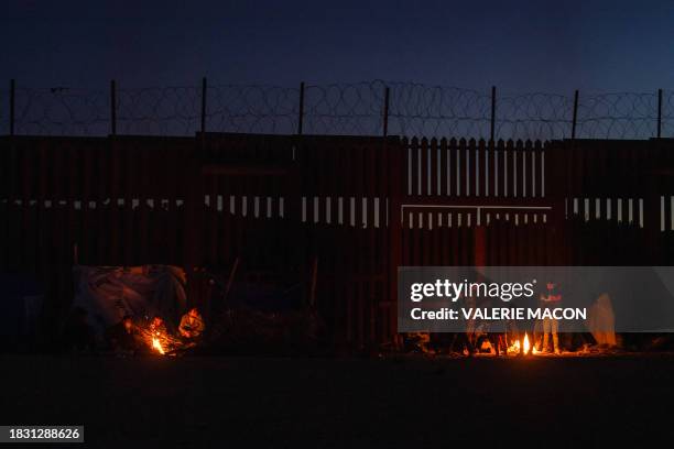 Newly arrived migrants attempt to stay warm by a fire as they spend the night in camp in front of the wall separating Mexico and the United States in...