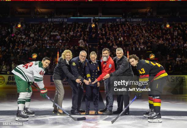 Quinn Hughes of the Vancouver Canucks and Jared Spurgeon of the Minnesota Wild pose for a ceremonial puck drop with the Chief of Vancouver fire,...