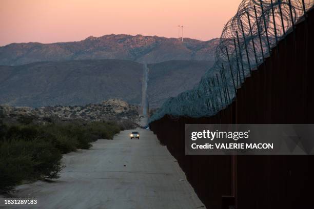 Car drives alongside the border fence at the US-Mexico border in Jacumba, California, December 6, 2023. Hundreds of migrants who cross into the...