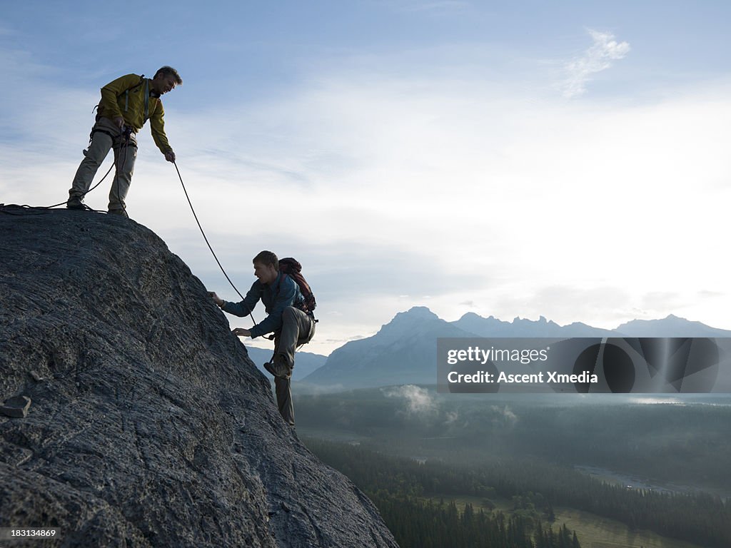 Father belays son up rock cliff above mountains