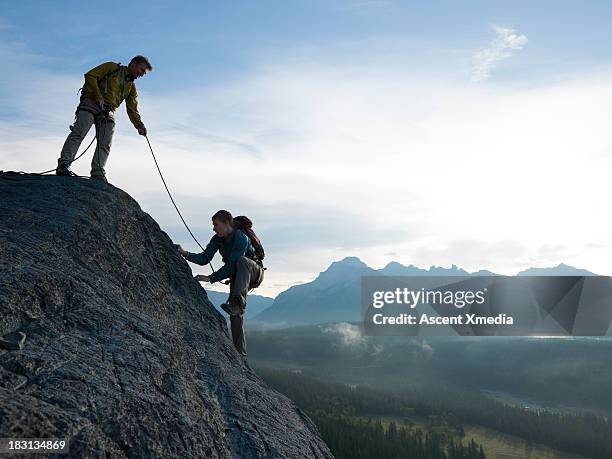 father belays son up rock cliff above mountains - trust stock pictures, royalty-free photos & images