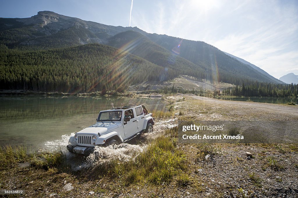 Two women pilot Jeep through lake shallows, mtns