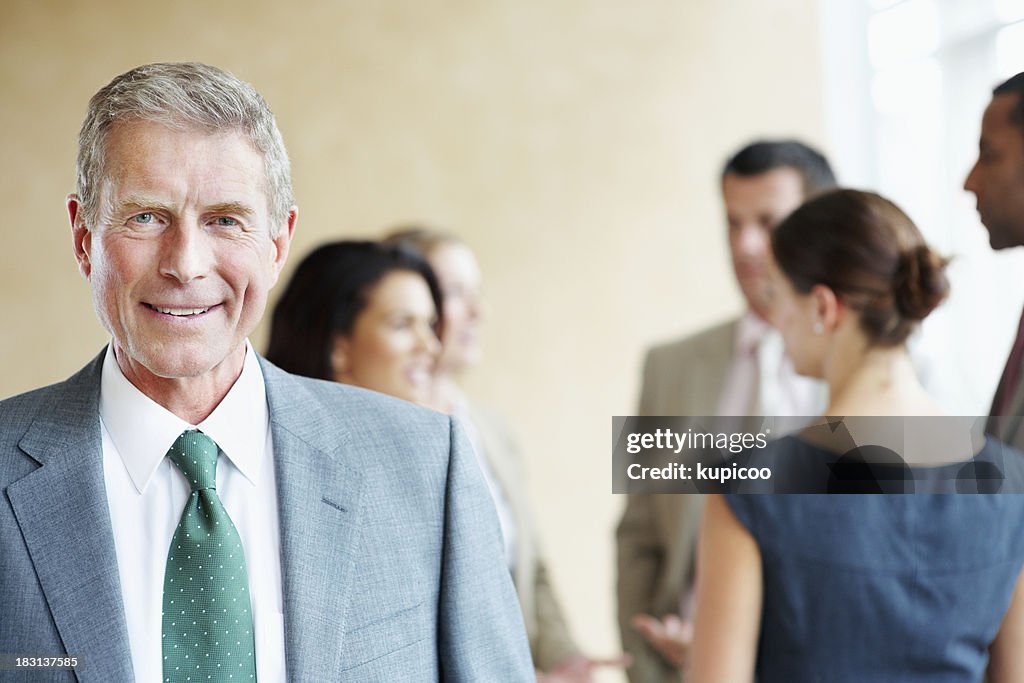 Smiling mature business man with his blur team in background