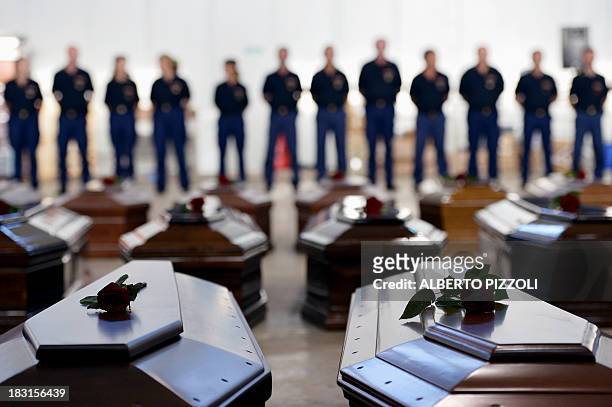 People stand next to Coffins of victims in a hangar of the Lampedusa airport on October 5, 2013 after a boat with migrants sank, killing more than...