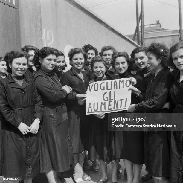 Workwomen on strike, three of them holding up a sign which reads "Vogliamo Gli Aumenti" , Milan, Italy, 1954. From the exhibition "Olives and bolts -...