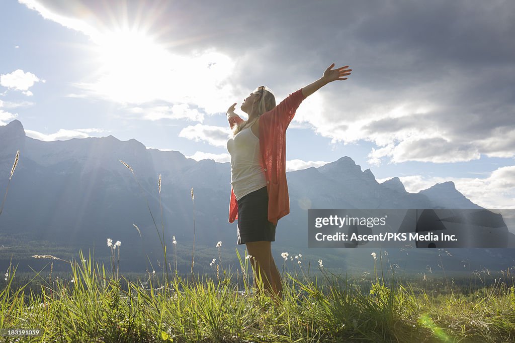 Woman stretches towards sunrise, mountain meadow