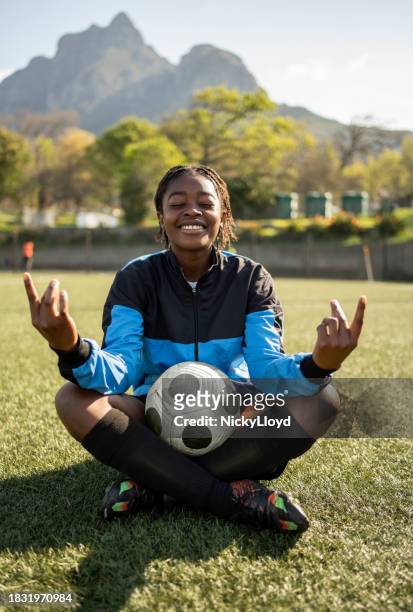 happy young african girl with a soccer ball sitting in lotus pose on sports field - yoga teen stock pictures, royalty-free photos & images