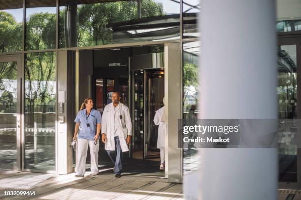 male and female medical professionals walking out from hospital building - sliding door exit stock pictures, royalty-free photos & images