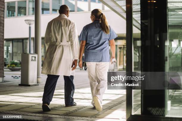 rear view of male and female healthcare workers walking near hospital building - sliding door exit stock pictures, royalty-free photos & images