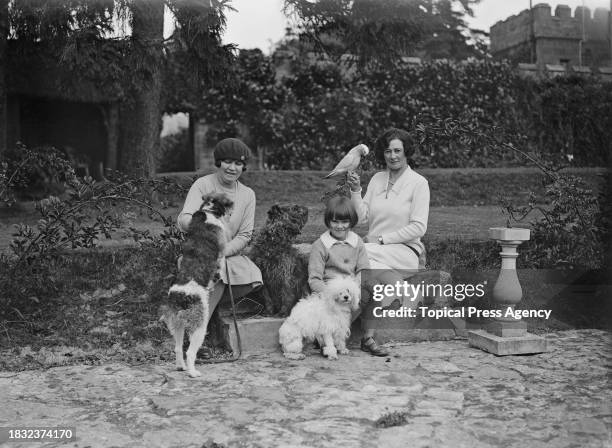 Tatton, her daughter Elizabeth Tatton and Madeleine Mary Pedder with dogs, including toy poodle Desiree, and a parrot sit on steps at Wadhurst Castle...