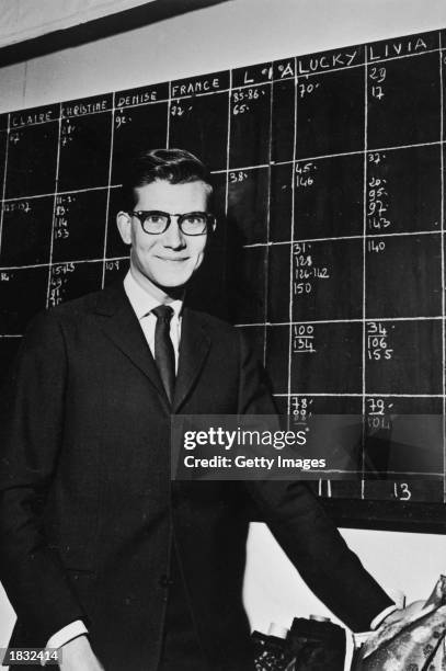 French fashion designer Yves Saint-Laurent poses by the moodel schedule in the atelier of the House of Christian Dior, Paris, France, 1958.