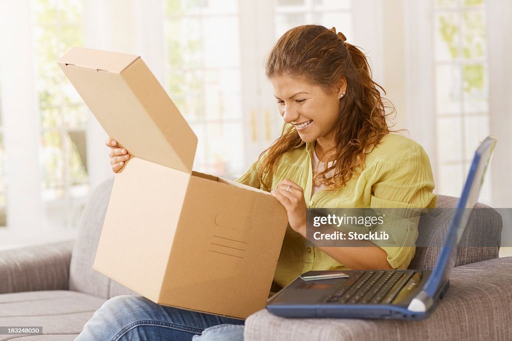 Happy young woman opening package at home