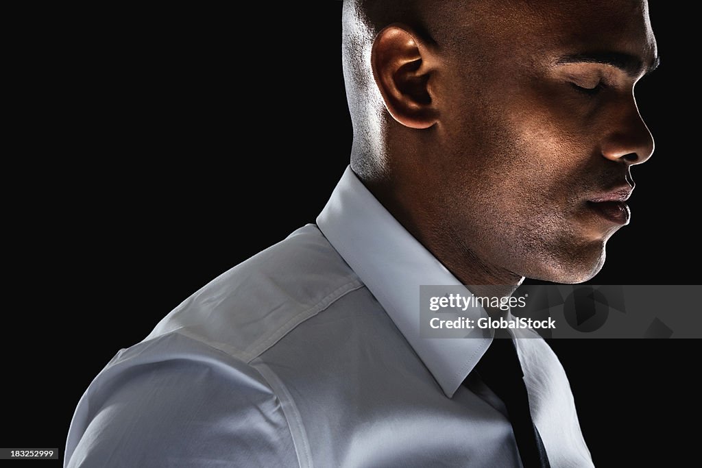 An African American business man with eyes closed against black