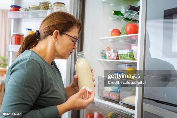 disgusted woman smelling expired milk by the fridge - menselijk lichaamsdeel stockfoto's en -beelden