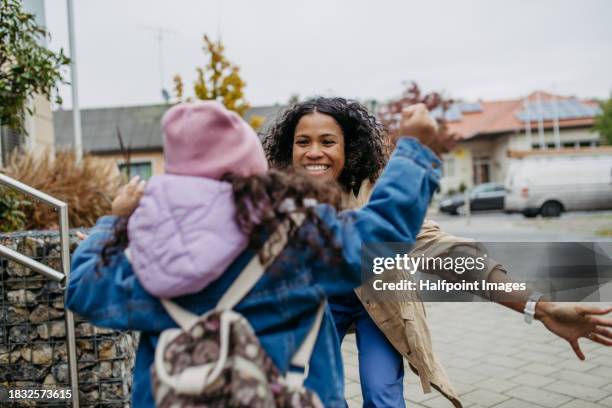 female nurse, doctor picking up small daughter from kindergarten, preschool, embracing in front school building. work-life balance of healthcare worker as parent and partner. - arrivée photos et images de collection
