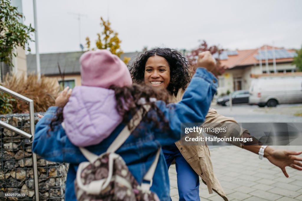 Female nurse, doctor picking up small daughter from kindergarten, preschool, embracing in front school building. Work-life balance of healthcare worker as parent and partner.