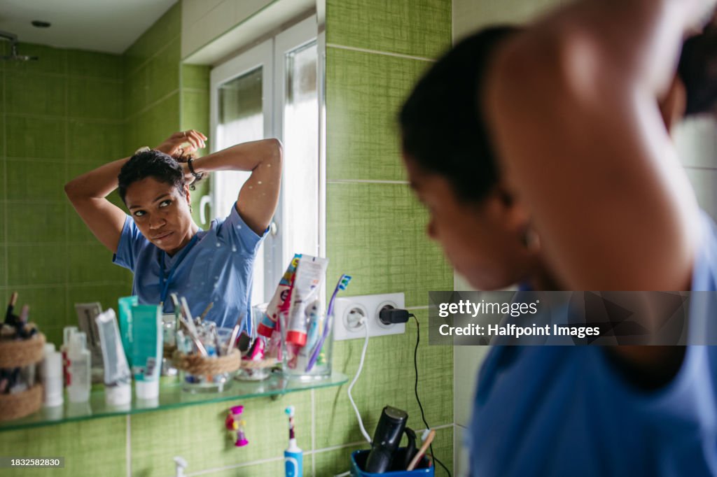 Female nurse or doctor getting ready for work in the morning, brushing hair, making ponytail in bathroom. Morning hair and skincare before leaving house, dressed in scrubs.