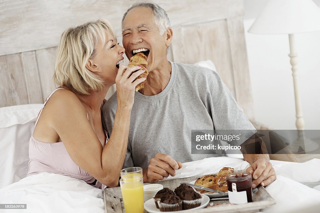 Mature woman feeding senior man while having breakfast in bed