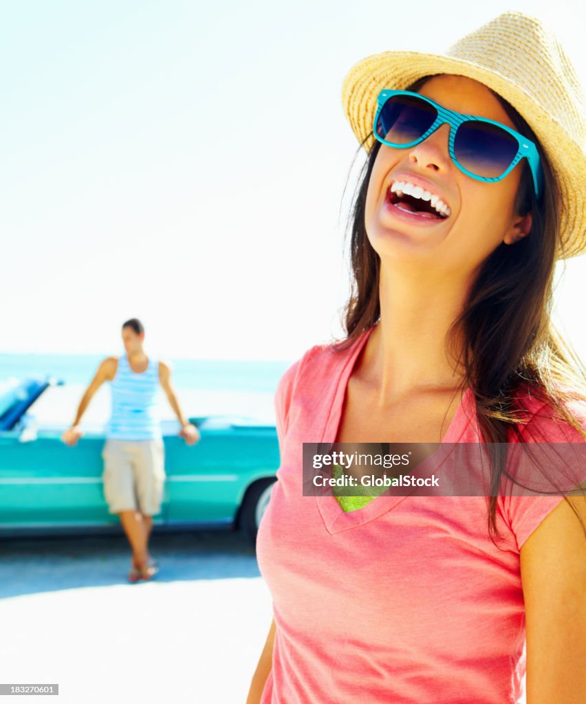 Joyful young woman wearing sunglasses with man in background