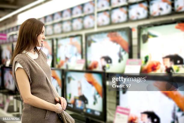 a woman looking at a wall of televisions for purchase - shopping centre screen stock pictures, royalty-free photos & images